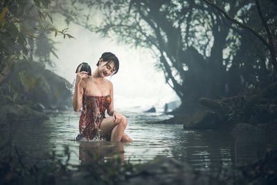 Full length of shirtless man sitting in water