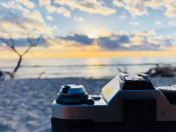 Close-up of camera at beach during sunset