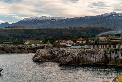 Scenic view of sea by buildings and mountains against sky