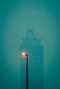 Illuminated tower by sea against sky at dusk