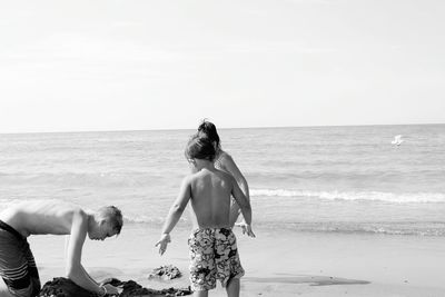 Siblings playing in sand on shore at beach against clear sky