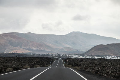 Empty road by mountains against sky