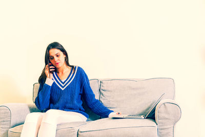 Young woman looking away while sitting on sofa