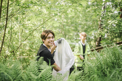 Portrait of smiling boy holding plastic garbage bag amidst plants