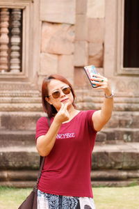 Woman taking selfie through mobile phone against building