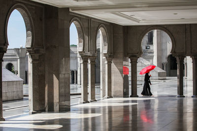 Side view of woman with umbrella walking against building