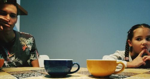 Siblings sitting at table against wall