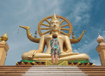 Low angle view of woman standing by buddha statue at temple against sky