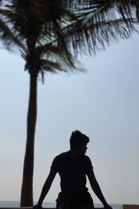 Silhouette man by palm tree against sky