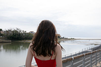 Rear view of woman standing on pier at beach against sky