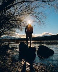 Rear view of silhouette man standing on rock in river during sunny day