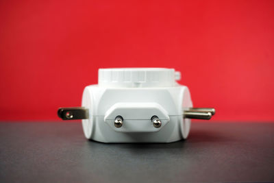 Close-up of electric plug on table against red background