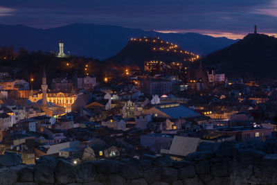 High angle view of illuminated buildings in city and hills at dusk
