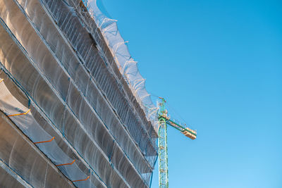 Low angle view of crane by building against clear blue sky