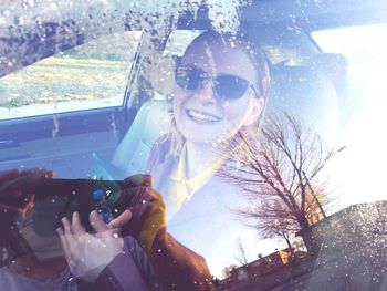 Portrait of young woman photographing through smart phone in car