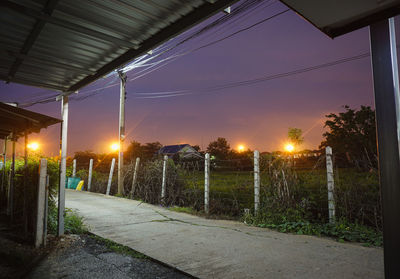 Illuminated street by road against sky during sunset