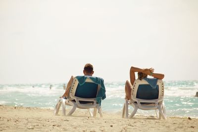 Rear view of couple sitting on beach against clear sky