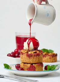 Cherry crumble pie decorated with a scoop of ice cream and poured with cherry sauce on a plate, whi