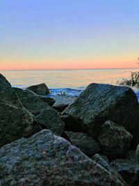 Rocks by sea against sky during sunset