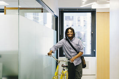 Portrait of happy businessman with bicycle standing in creative office