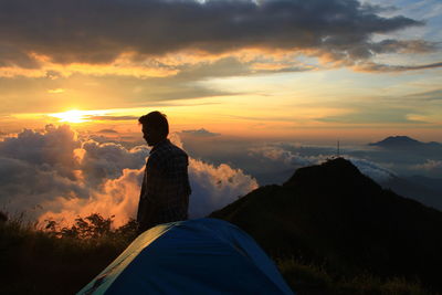 Man campint on top of a hill at sunset