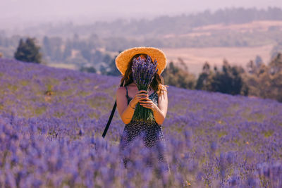 Woman in a straw hat closing her face with a bouquet of lavender flowers in a field