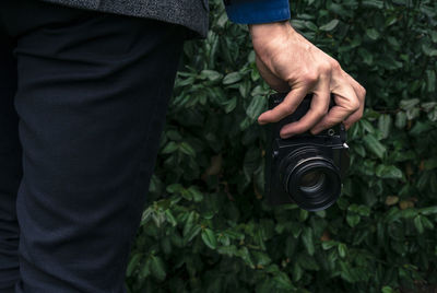 Midsection of man holding camera against plants