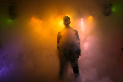 Man standing amidst illuminated smoke on stage