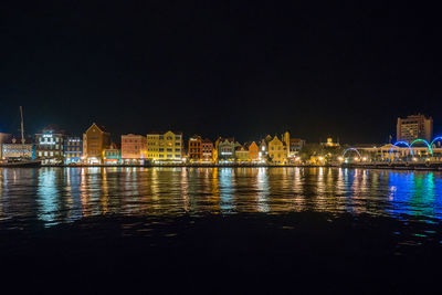 Illuminated buildings by river against sky at night