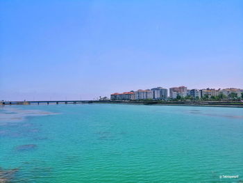 Scenic view of sea by buildings against clear blue sky