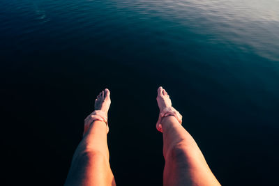 Cropped hands holding woman legs over sea