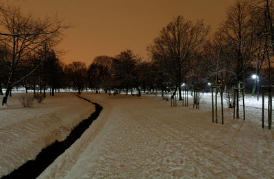 Bare trees on snow covered field against sky