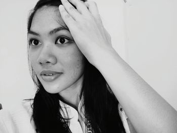 Close-up of smiling young woman with hand in hair against wall