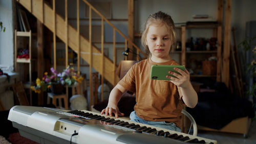 Smiling girl holding mobile and playing piano