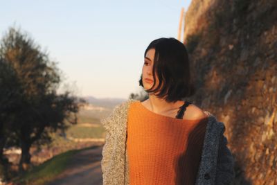 Thoughtful young woman looking away while standing against sky