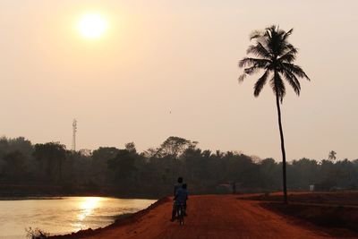 Rear view of men bicycling on dirt road by lake