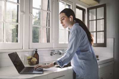 Side view of female professional using laptop on counter at home office