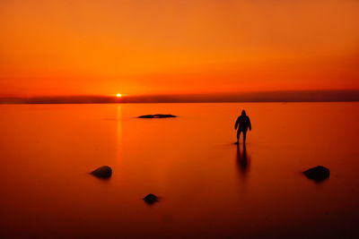 Silhouette woman standing at beach against sky during sunset