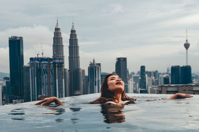 Woman relaxing in swimming pool against buildings in city