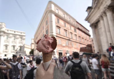 Cropped hand holding ice cream on street in city