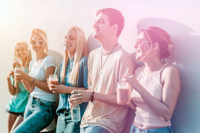 Group of friends drinking smoothies while standing by the wall