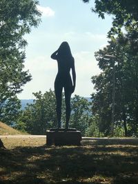 Statue of man standing by tree against sky