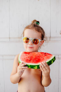 Portrait of shirtless girl eating watermelon against wall