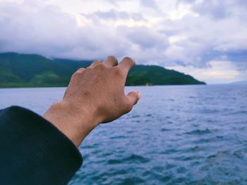 Close-up of hand against sea against sky