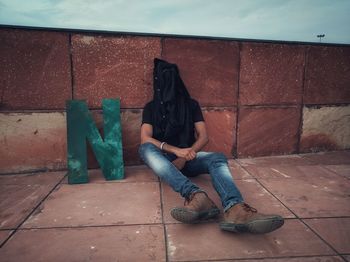 Full length of man sitting by wall