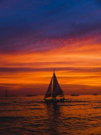 Sailboat sailing on sea against orange sky