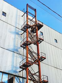 Low angle view of crane by building against sky