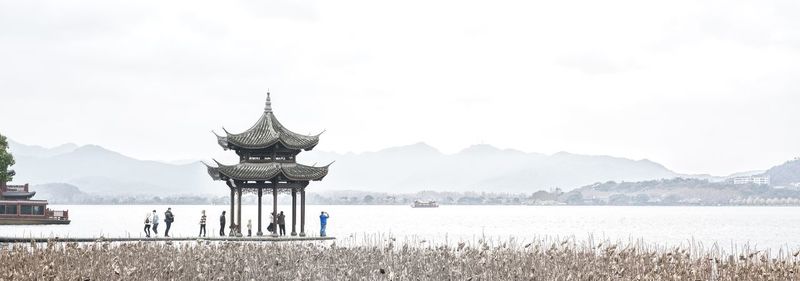 People standing on built structure by lake against sky