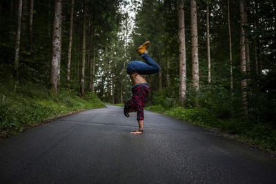 Full length side view of man doing handstand on road amidst forest