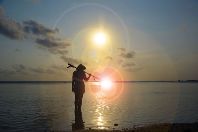 Silhouette man standing in sea against sky during sunset